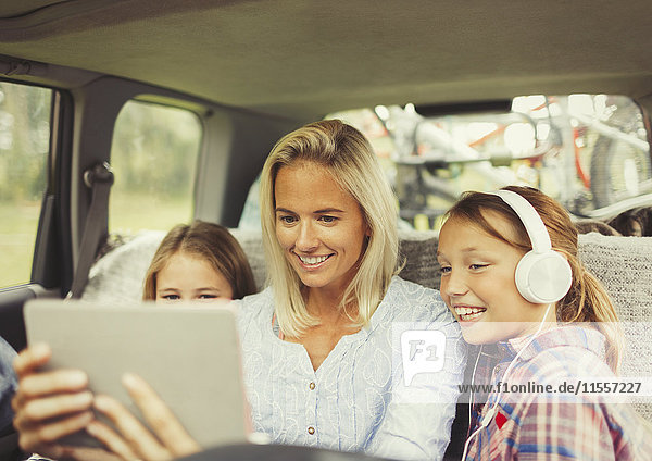 Mutter und Töchter beim Anschauen des Videos auf dem digitalen Tablett auf dem Rücksitz des Autos