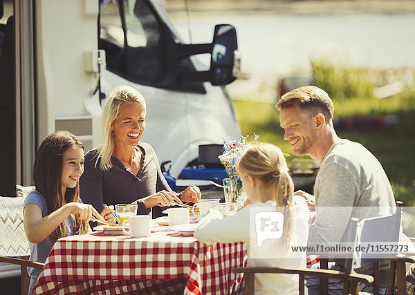 Family enjoying breakfast at table outside sunny motor home