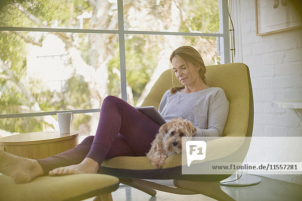 Frau mit Hund  die sich auf einem Stuhl mit digitalem Tablet entspannt