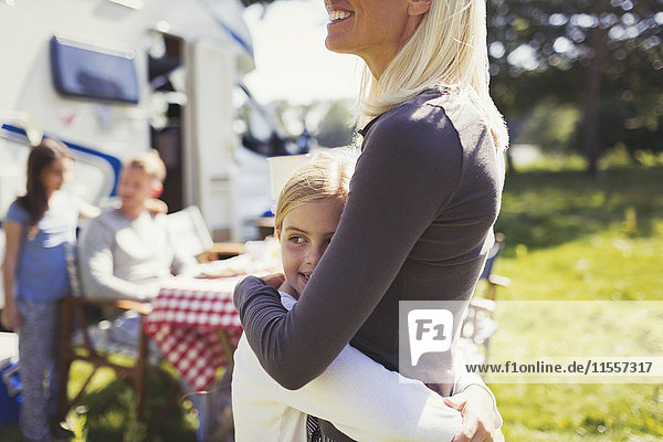 Mother and daughter hugging outside sunny motor home