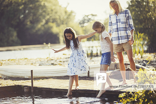 Mutter beobachtet Töchter  die Zehen im Wasser am Ufer des Sees kleben.