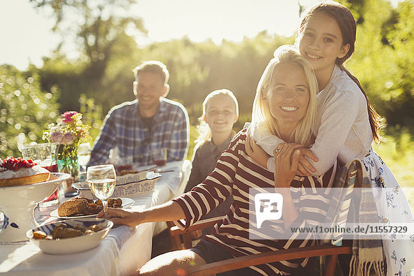 Portrait lächelnd liebevolle Mutter und Tochter umarmend am sonnigen Gartenparty-Tisch