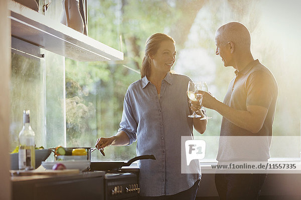 Couple toasting white wine glasses  cooking in kitchen