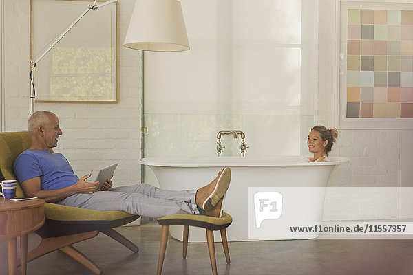 Ehemann mit digitalem Tablet entspannt sich  spricht mit Frau in der Badewanne in einem Luxushotelzimmer
