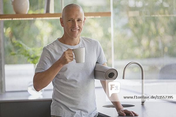 Portrait lächelnder reifer Mann mit Yogamatte trinkt Kaffee in der Küche