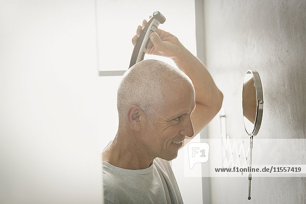 Älterer Mann rasiert sich den Kopf mit einem elektrischen Rasierapparat im Badezimmer