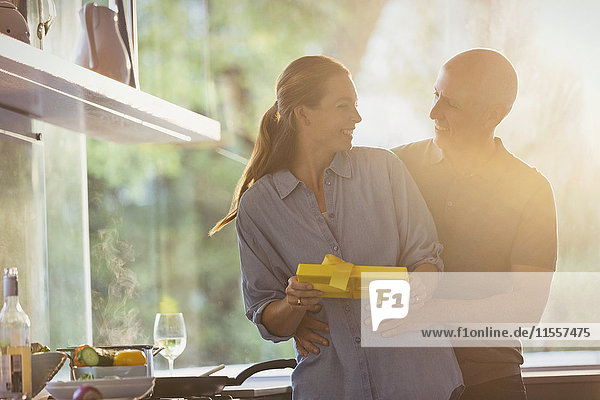 Lächelnder Ehemann überrascht Frau mit Geschenk in sonniger Küche