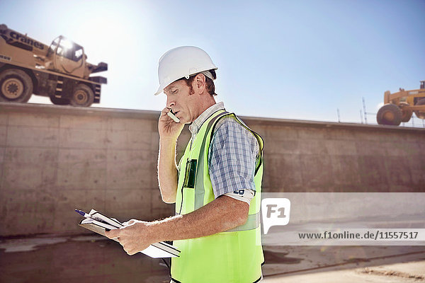 Bauarbeiter-Vorarbeiter im Gespräch am Handy auf der sonnigen Baustelle
