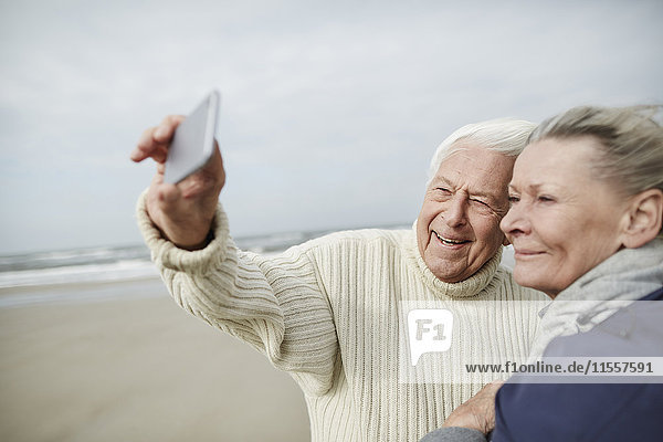Senior Paar nimmt Selfie mit Handy am windigen Winterstrand