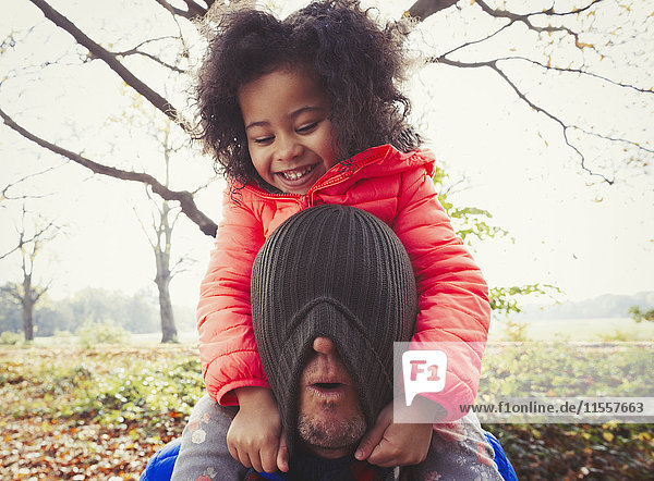 Verspielte Tochter zieht Strumpfmütze über das Gesicht des Vaters im Herbstpark