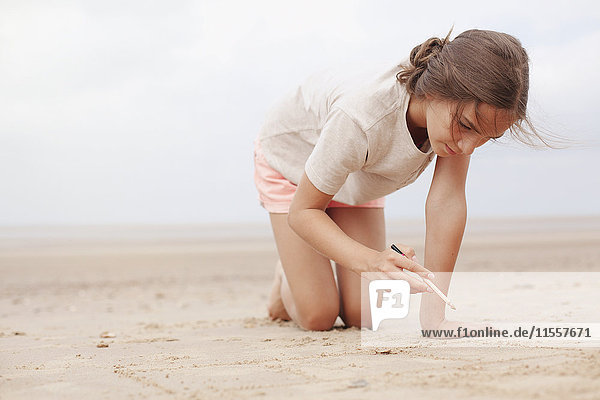 Mädchen mit Stock schreiben in Sand auf bewölktem Sommerstrand