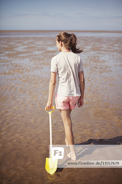 Teenager-Mädchen schleppt Schaufel im nassen Sand am sonnigen Sommerstrand