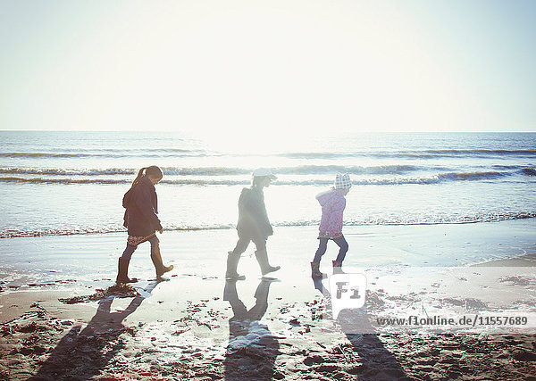 Bruder und Schwestern in warmer Kleidung gehen im nassen Sand am sonnigen Strand spazieren