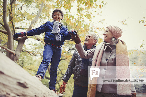 Großeltern gehender Enkel auf Baumstamm im Herbstpark