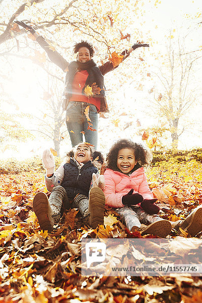 Verspielte Mutter und Töchter werfen Herbstlaub im sonnigen Park