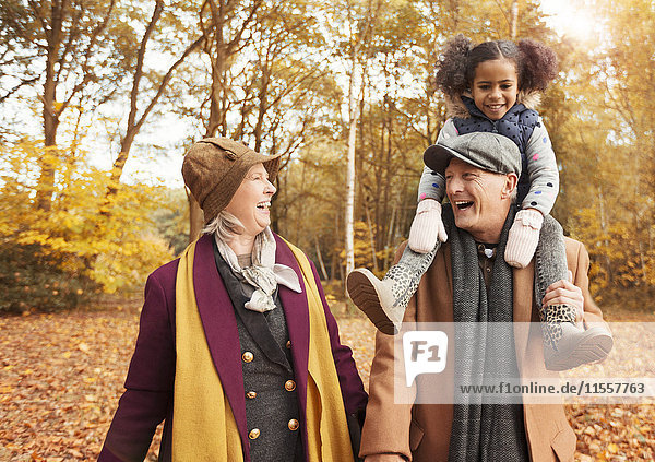 Laughing senior couple carrying daughter on shoulders in autumn woods
