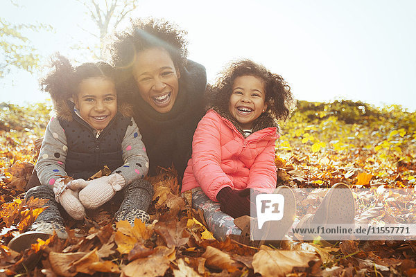 Portrait verspielte Mutter und Töchter im Herbstlaub im sonnigen Park