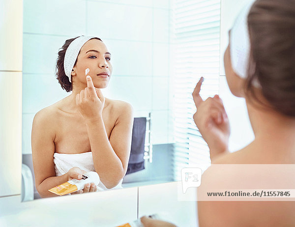 Woman applying moisturizer to cheek at bathroom mirror