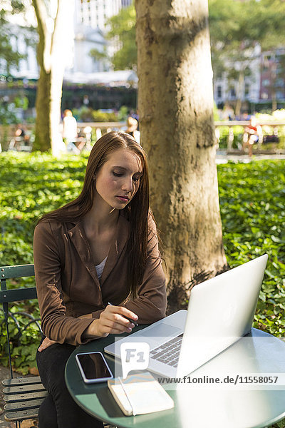 USA  New York  Manhattan  nachdenkliche junge Geschäftsfrau am Tisch im Park mit Laptop