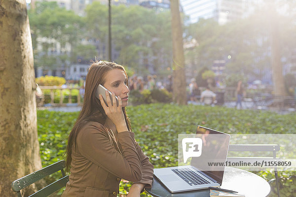 USA  New York  Manhattan  junge Geschäftsfrau am Telefon am Tisch im Park