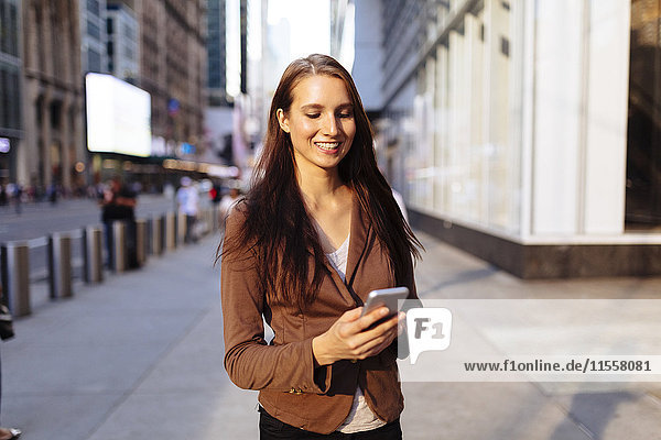 USA  New York  Manhattan  lächelnde junge Geschäftsfrau beim Blick aufs Handy