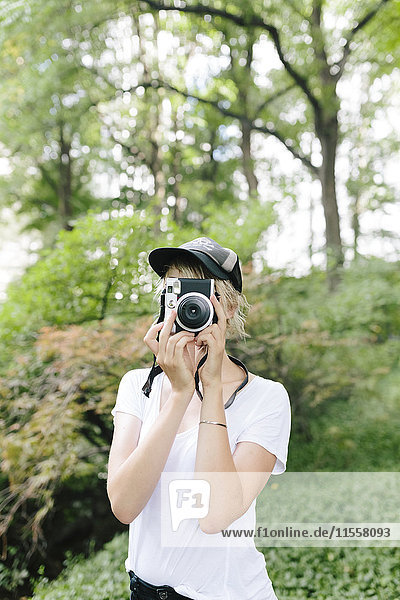Junge Frau mit einer Vintage-Kamera beim Fotografieren im Park