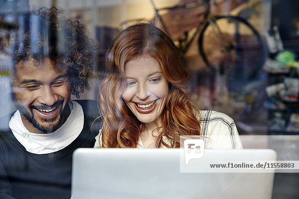Glückliches junges Paar mit Laptop hinter der Fensterscheibe