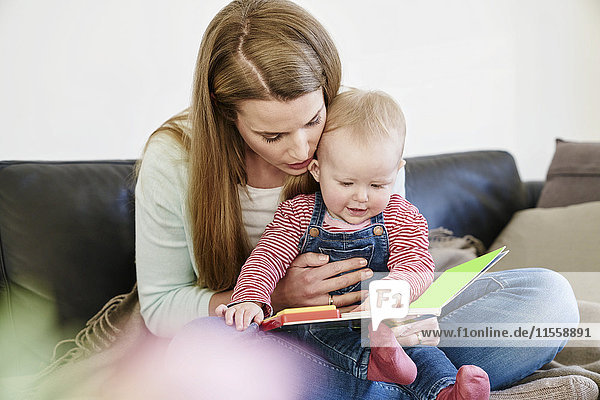 Mutter und kleines Mädchen zu Hause beim Betrachten des Buches