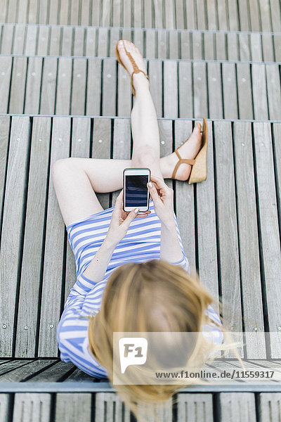 Junge Frau am Pier sitzend mit dem Handy