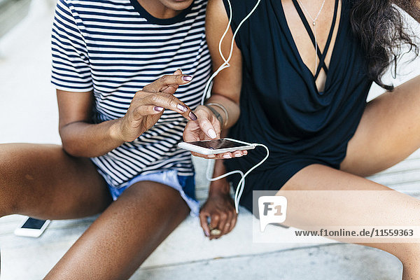 Zwei Freunde sitzen auf der Treppe und hören Musik zusammen mit Kopfhörern und Smartphone  Teilansicht