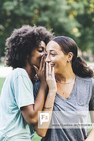 Two young women whispering in a park