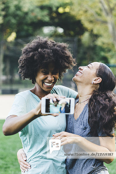 Two happy best friends taking selfie with smartphone in a park