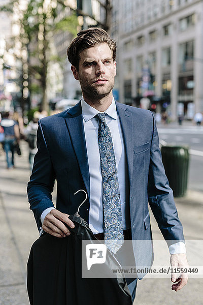 Handsome businessman walking in Manhattan  carrying jacket on a hanger