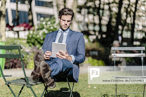 Businessman in Manhattan sitting on garden chair using digital tablet with feet up