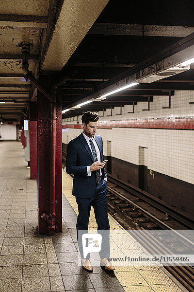 Businessman standing at a New York metro station using smart phone