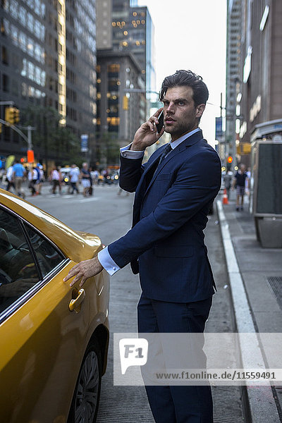 Geschäftsmann am Telefon  der in ein Taxi in Manhattan einsteigt.