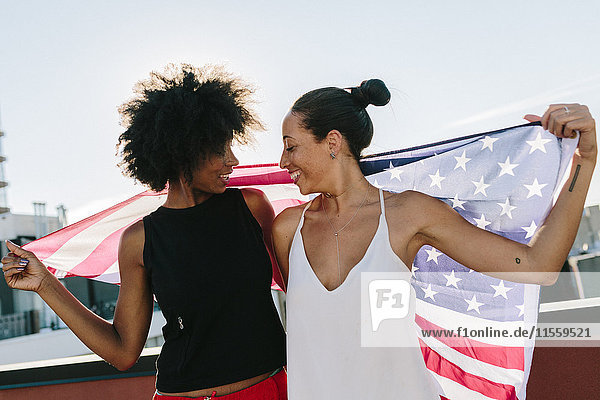 Female friends holding US American flag  standing on rooftop