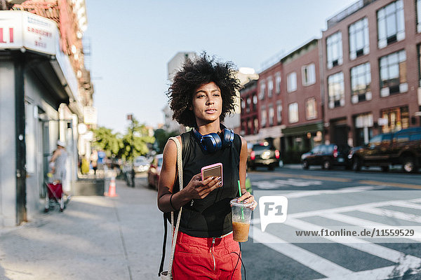 Junge Frau mit Kopfhörer und Smartphone Crossong Street in Brooklyn  carying take away drink