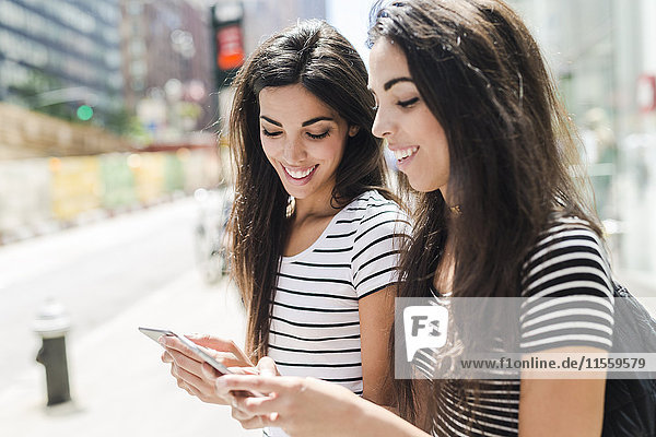 USA  New York City  zwei glückliche Zwillingsschwestern beim Blick auf Handys in Manhattan