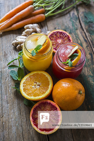 Zwei Gläser mit verschiedenen Orangensäften  Orangen  Karotten  Minzeblättern und Ingwer.