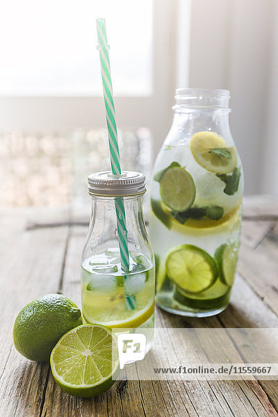 Glasflaschen mit aufgegossenem Wasser mit Zitrone  Limette  Minzeblättern und Eiswürfeln