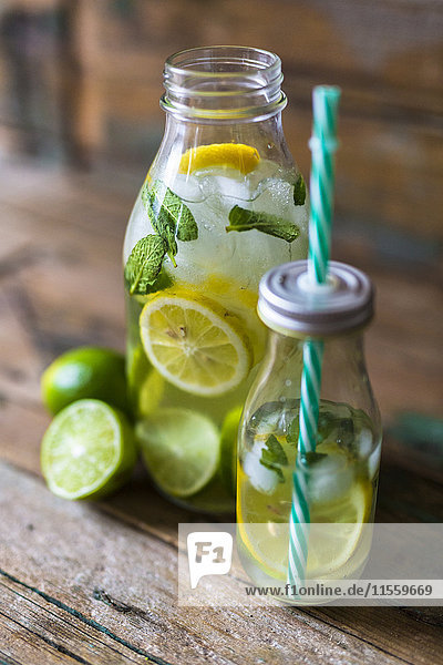 Glasflaschen mit aufgegossenem Wasser mit Zitrone  Limette  Minzeblättern und Eiswürfeln