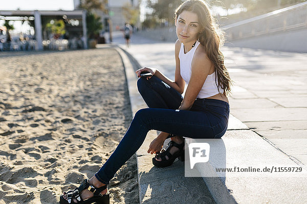 Portrait of young woman sitting on beach promenade at sunset