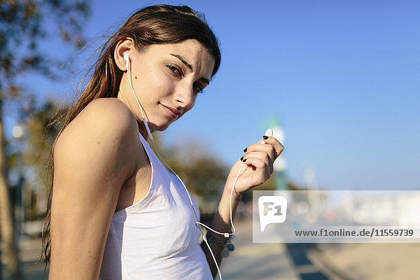 Young woman relaxing on beach promenade at sunset listening music with earphones