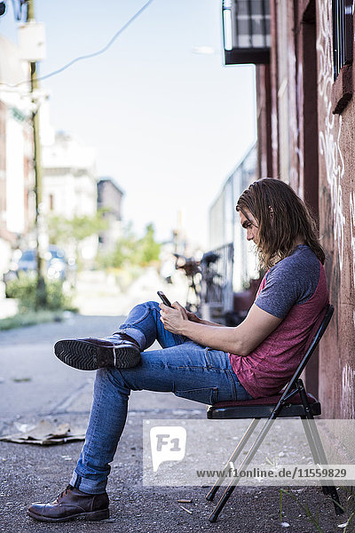 USA  New York City  Mann auf einem Stuhl sitzend mit Handy in Williamsburg  Brooklyn