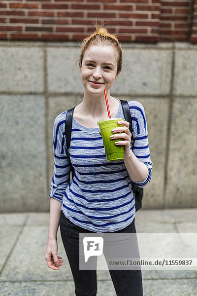 Porträt einer lächelnden jungen Frau  die einen Smoothie im Freien trinkt.