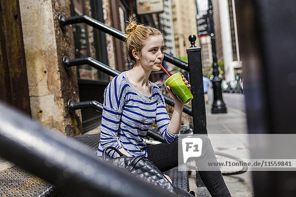 USA  New York City  woman sitting on stoop drinking a smoothie in Manhattan