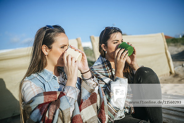 Two young women drinking coffee on the beach