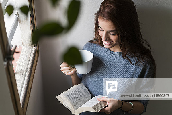 Attractive young woman reading book and drinking coffee