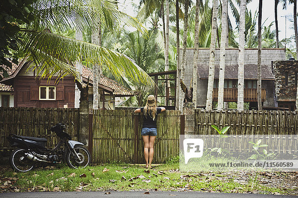 Indonesien  Java  Rückansicht einer Frau  die sich auf das Gartentor stützt und Häuser betrachtet.